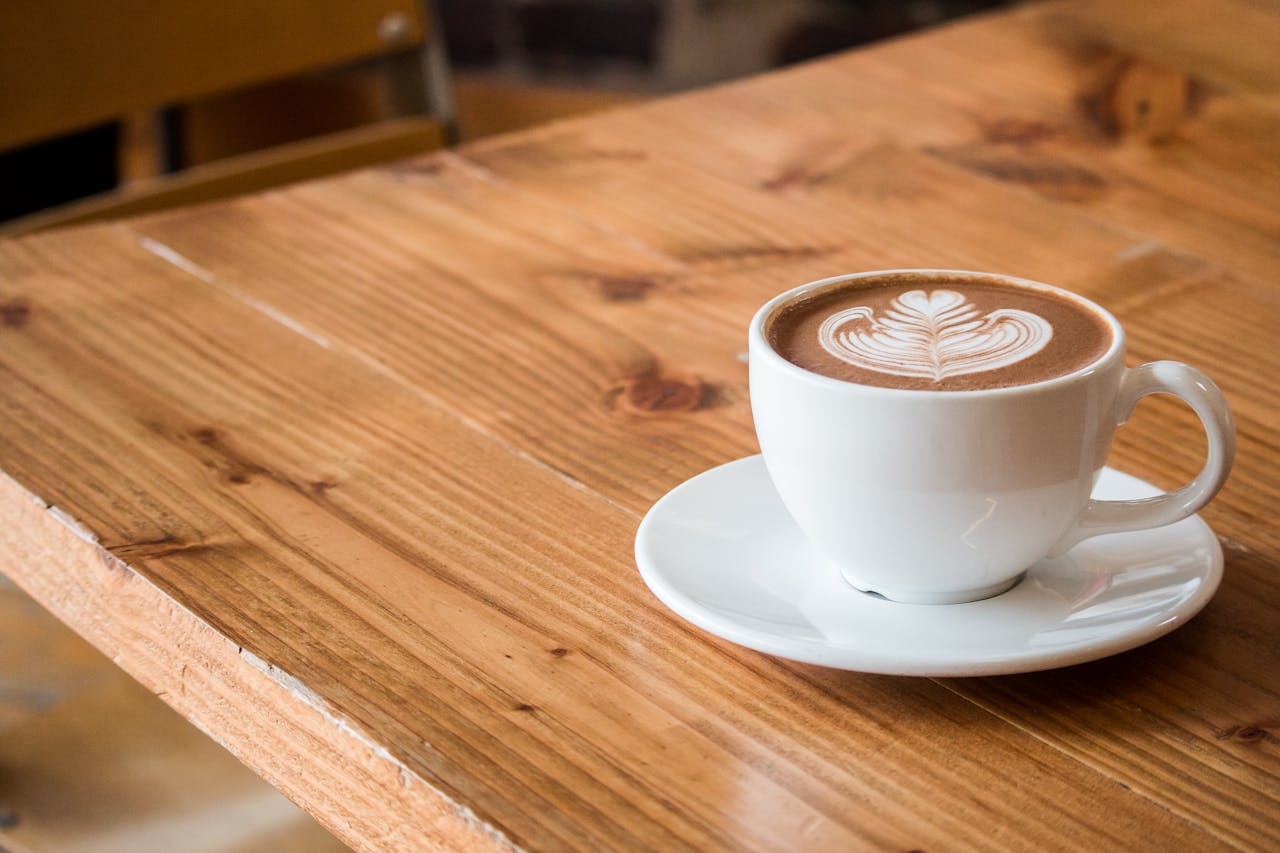team-01 Close-up of a white cup of latte with artistic foam on a rustic wooden table.