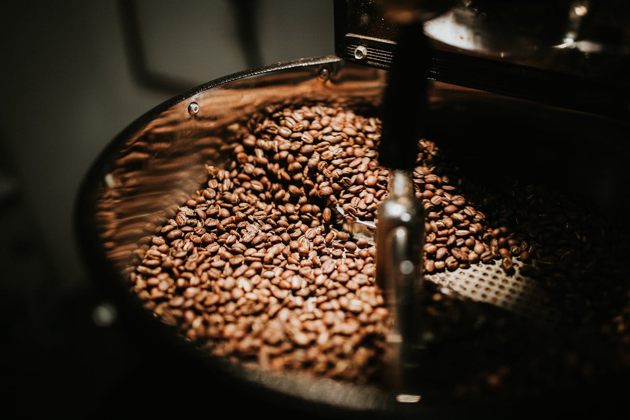 team-02 Close-up of freshly roasted coffee beans in a large industrial coffee roaster, showcasing rich textures and warm tones.